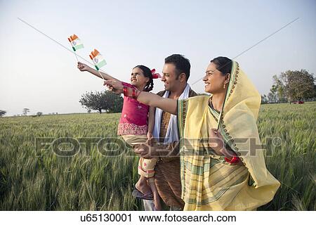Stock Image - Rural family standing in the field holding Indian flag . Fotosearch