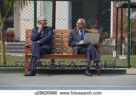 Senior businessmen looking at each other while using cell phone and laptop View Large Photo Image Stock Photograph - Senior businessmen looking at each other while using cell phone and laptop . Fotosearch