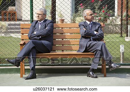 Senior male business executives looking away with arms crossed while sitting on bench in a tennis court View Large Photo Image Stock Image - Senior male business executives looking away with arms crossed while sitting on bench in a tennis court . Fotosearch