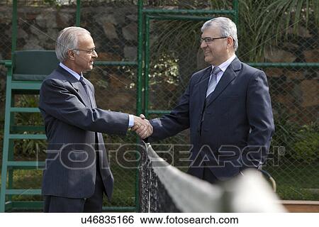 Senior male professionals looking at each other while shaking hands over tennis net in court View Large Photo Image Stock Photograph - Senior male professionals looking at each other while shaking hands over tennis net in court . Fotosearch