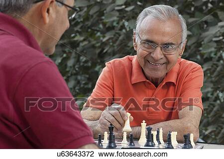 Senior man smiling at friend while holding chess piece View Large Photo Image Stock Image - Senior man smiling at friend while holding chess piece . Fotosearch