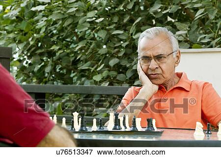 Stock Photo - Senior man with hand on chin looking at chess board and thinking of his next move . Fotosearch
