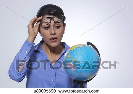 Shocked businesswoman looking at globe over glasses against gray background View Large Photo Image Stock Image - Shocked businesswoman looking at globe over glasses against gray background. Fotosearch
