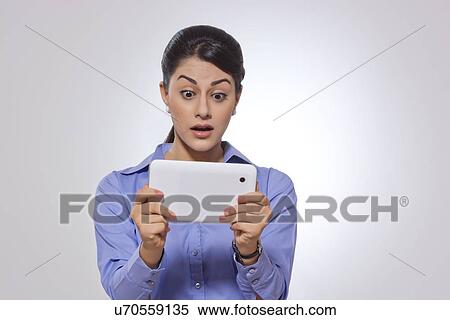 Stock Photography - Shocked businesswoman using digital tablet over gray background. Fotosearch