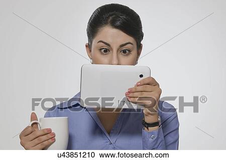 Shocked businesswoman with coffee mug looking at digital tablet over gray background View Large Photo Image Stock Image - Shocked businesswoman with coffee mug looking at digital tablet over gray background. Fotosearch