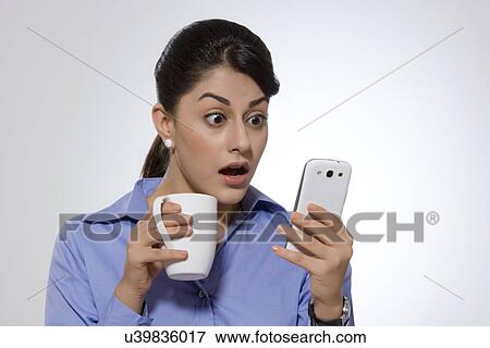 Shocked businesswoman with coffee mug reading text message on smart phone against gray background View Large Photo Image Stock Photo - Shocked businesswoman with coffee mug reading text message on smart phone against gray background. Fotosearch