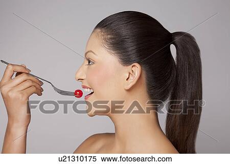 Stock Photography - Side view of a woman eating cherry tomato on fork . Fotosearch