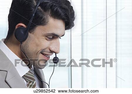 Stock Image - Side view of businessman wearing headset in office. Fotosearch