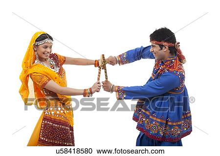 Stock Image - Side view of happy couple performing Dandiya Raas against white background. Fotosearch