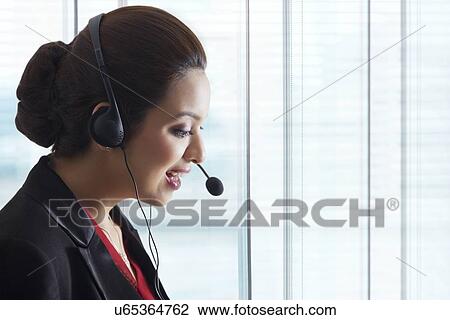 Stock Image - Side view of young female call center representative in office. Fotosearch