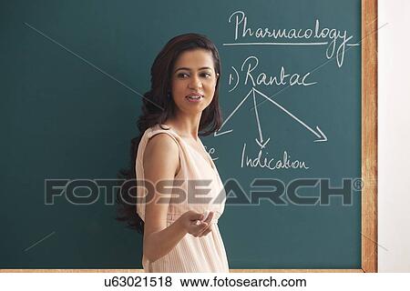 Side view of young female teacher explaining a lesson against green board View Large Photo Image Stock Photo - Side view of young female teacher explaining a lesson against green board . Fotosearch