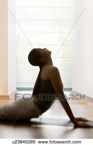 Stock Photo - Side view of young woman doing yogic 'sun salutation' on mat. Fotosearch