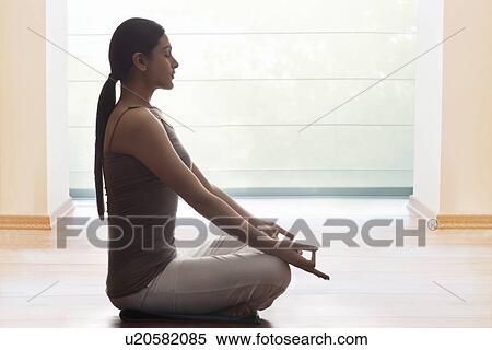 Stock Photography - Side view of young woman meditating on floor. Fotosearch