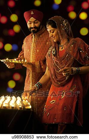 Stock Image - Sikh man holding a tray of diyas while the woman places them on a table . Fotosearch