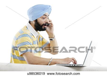 Sikh man talking on the phone while working on a laptop View Large Photo Image Stock Photo - Sikh man talking on the phone while working on a laptop . Fotosearch