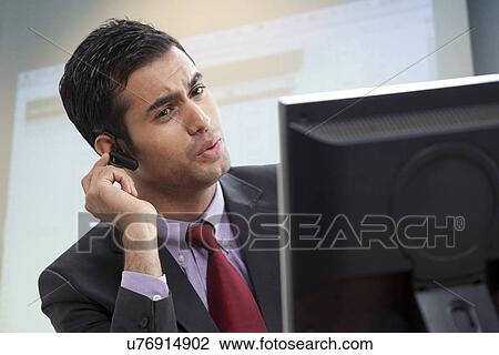 Stock Image - Smart male executive looking at computer while conversing on call . Fotosearch