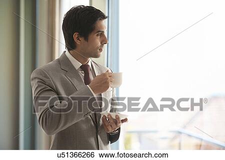 Stock Photograph - Smart young businessman having cup of tea while thinking . Fotosearch