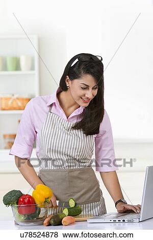 Smiling businesswoman surfing on laptop while preparing food in kitchen at home View Large Photo Image Stock Photo - Smiling businesswoman surfing on laptop while preparing food in kitchen at home. Fotosearch