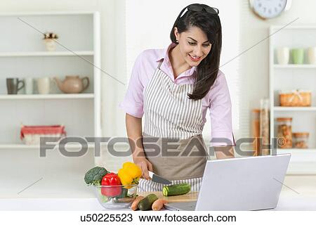 Smiling businesswoman using laptop while preparing food in kitchen View Large Photo Image Stock Image - Smiling businesswoman using laptop while preparing food in kitchen. Fotosearch