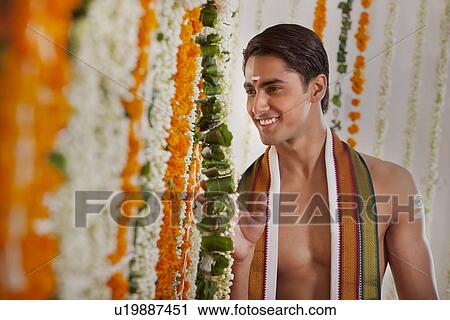 Stock Image - Smiling groom looking through garlands . Fotosearch