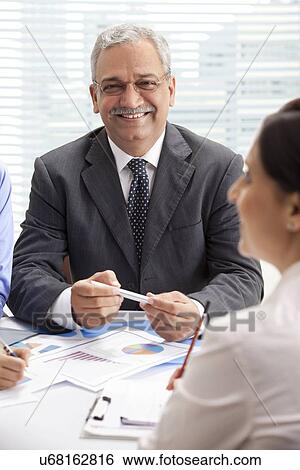 Stock Photograph - Smiling mature businessman in discussion with female executives . Fotosearch