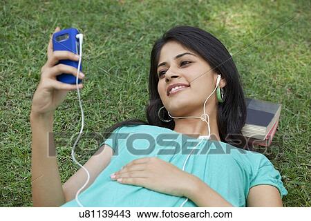 Smiling woman lying on grass listening to mp3 player View Large Photo Image Stock Image - Smiling woman lying on grass listening to mp3 player . Fotosearch