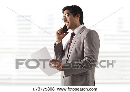 Smiling young businessman on phone call with a document View Large Photo Image Stock Photo - Smiling young businessman on phone call with a document . Fotosearch