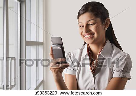 Smiling young businesswoman text messaging at office View Large Photo Image Stock Photo - Smiling young businesswoman text messaging at office . Fotosearch