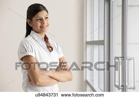 Smiling young businesswoman thinking with arms crossed at office View Large Photo Image Stock Image - Smiling young businesswoman thinking with arms crossed at office . Fotosearch
