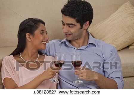 Smiling young couple holding wineglass while looking at each other View Large Photo Image Stock Photo - Smiling young couple holding wineglass while looking at each other . Fotosearch