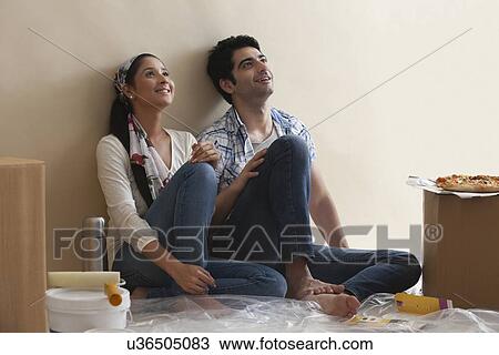 Stock Image - Smiling young couple leaning against the wall while thinking . Fotosearch