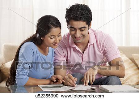 Stock Image - Smiling young couple solving crossword newspaper together . Fotosearch