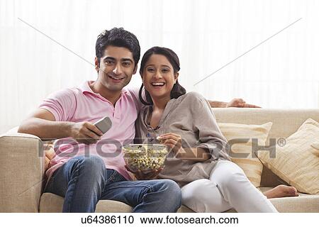 Stock Image - Smiling young couple watching TV while eating popcorn . Fotosearch
