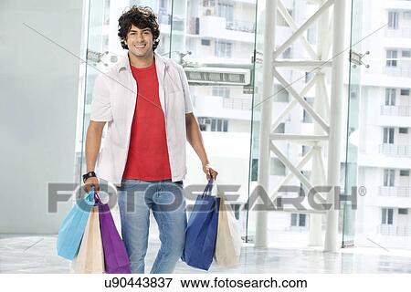 Stock Photo - Smiling young man carrying shopping bags . Fotosearch