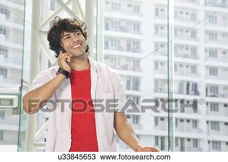 Smiling young man conversing on mobile phone View Large Photo Image Stock Image - Smiling young man conversing on mobile phone . Fotosearch