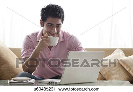 Smiling young man using laptop while having a cup of coffee View Large Photo Image Stock Image - Smiling young man using laptop while having a cup of coffee . Fotosearch
