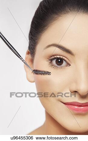 Stock Photograph - Smiling young woman applying mascara . Fotosearch