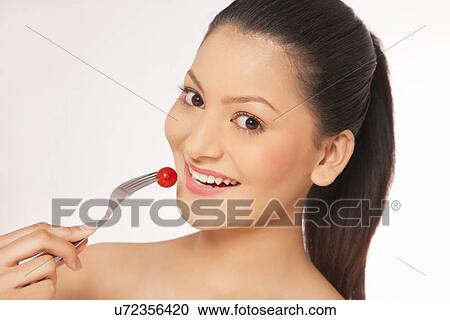 Smiling young woman eating cherry tomato on fork View Large Photo Image Stock Image - Smiling young woman eating cherry tomato on fork . Fotosearch