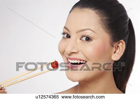 Smiling young woman eating cherry tomato with chop sticks View Large Photo Image Stock Photography - Smiling young woman eating cherry tomato with chop sticks . Fotosearch