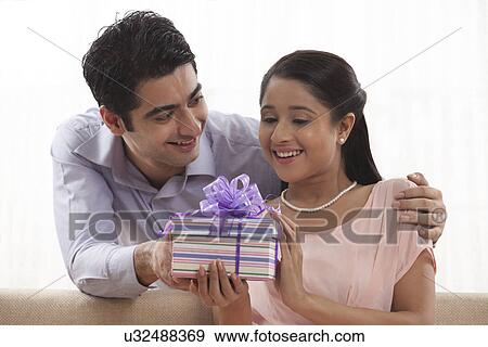 Stock Photo - Smiling young woman receiving gift from man at home . Fotosearch