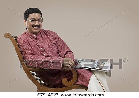 South Indian man sitting on a chair with a newspaper View Large Photo Image Stock Photo - South Indian man sitting on a chair with a newspaper . Fotosearch