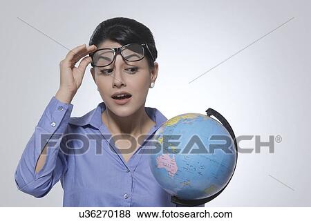 Surprised businesswoman looking at globe over glasses against gray background View Large Photo Image Stock Photo - Surprised businesswoman looking at globe over glasses against gray background. Fotosearch