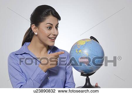Stock Image - Surprised businesswoman pointing at globe against gray background. Fotosearch