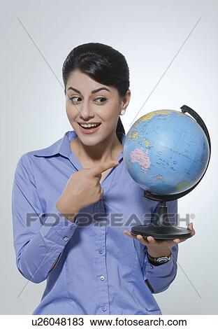 Stock Image - Surprised businesswoman pointing at globe against gray background. Fotosearch