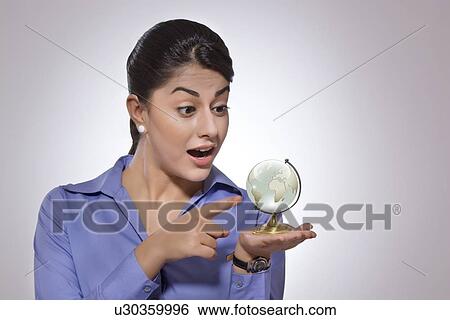 Stock Photograph - Surprised businesswoman pointing at crystal globe over gray background. Fotosearch