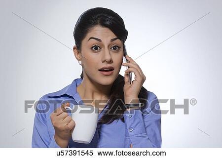 Surprised businesswoman with coffee mug using phone against gray background View Large Photo Image Stock Photography - Surprised businesswoman with coffee mug using phone against gray background. Fotosearch