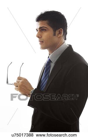 Stock Photo - Thoughtful businessman holding glasses over white background . Fotosearch
