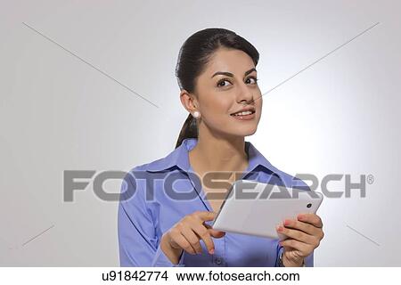 Picture - Thoughtful businesswoman holding digital tablet against gray background. Fotosearch