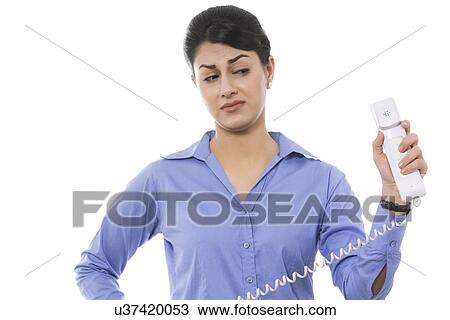 Stock Image - Thoughtful businesswoman holding telephone receiver against white background. Fotosearch