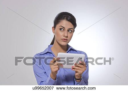 Stock Photo - Thoughtful businesswoman holding digital tablet over gray background. Fotosearch